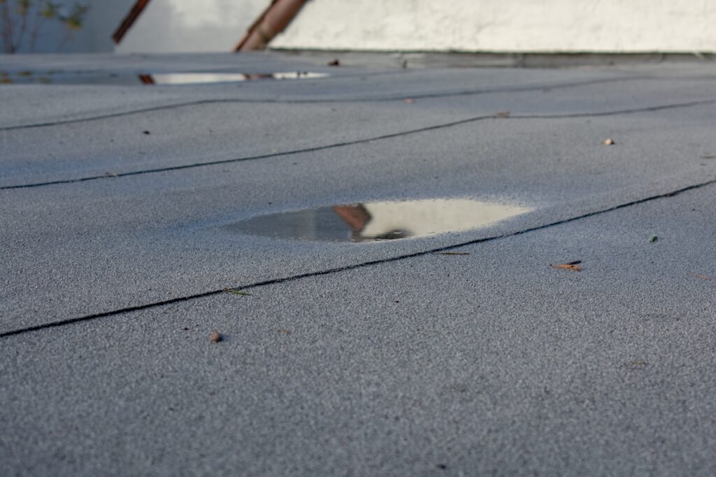 Ponding rainwater on flat roof after rain, roof drainage and leak problem.