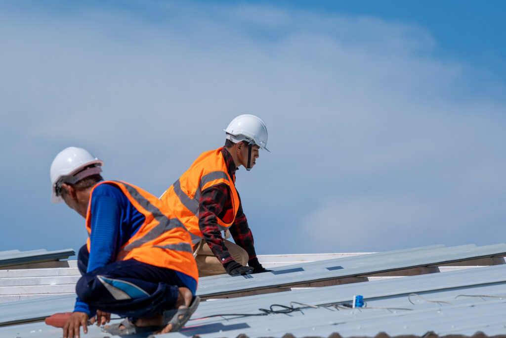 Roofer worker in protective uniform wear and gloves working installing metal sheet on top of the new roof at construction site.