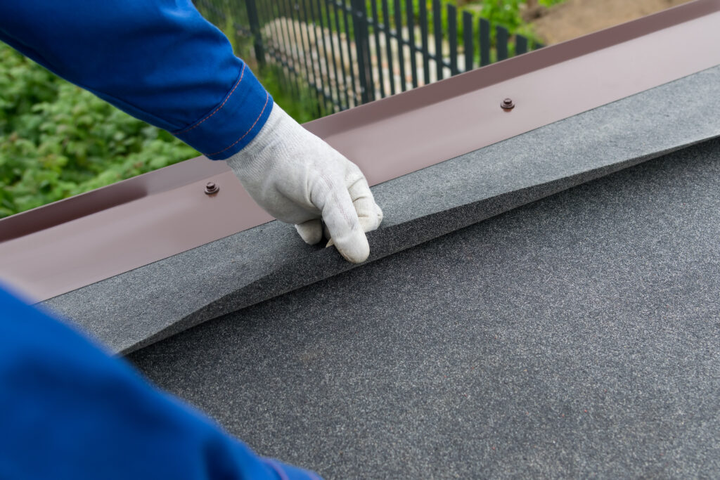 hands of a worker, checks the correctness of laying the material under soft tiles, close-up roofing material