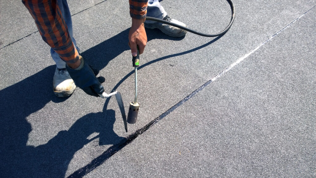 Roofer preparing part of bitumen roofing felt roll for melting by gas heater torch flame