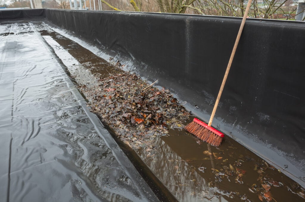 el niño 2026 hurricane season The gutter of a flat roof is full of debris from the trees such as leaves and branches, whit shovel, brush it will clean